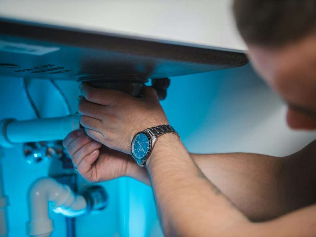 Hands working on a leaking supply line under a sink